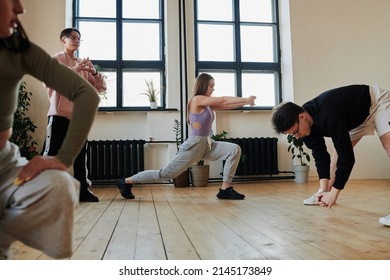 Contemporary Teenagers Doing Stretching Exercises On Wooden Floor Of Studio Or Dance Hall Before Repetition Of Vogue Dancing