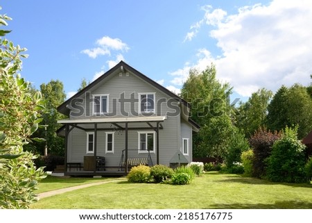 Contemporary two-story house of timber in countryside in summer. House have nice landscaping, with shrubs, green lawn and blooming trees. Russian dacha in Moscow region.