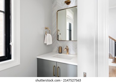 Contemporary White and Gray Half Bathroom. Gray bathroom vanity with gold fixtures and mirror showing into hallway.