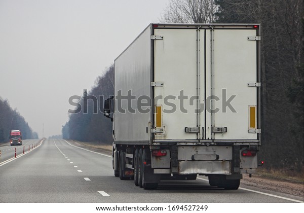 Contemporary\
white semi truck on empty two-lane road at spring day,\
international cargo logistics goods\
delivery