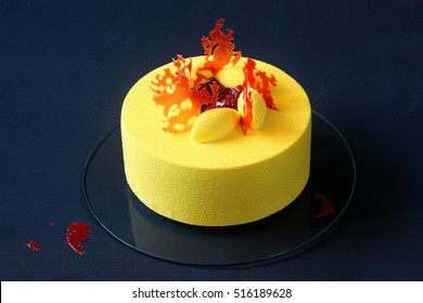 Contemporary Yellow Velvet Mousse Cake Decorated With Red Caramel And Wild Strawberries, On Dark Blue Background.