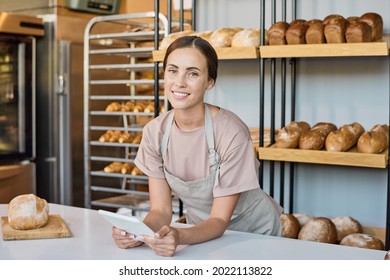 Contemporary young female clerk of bakery using tablet while scrolling through new assortment - Powered by Shutterstock