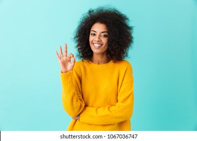 Content american woman in colorful shirt smiling on camera and gesturing ok sign isolated over blue background