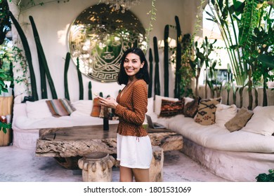 Content Asian Female Freelancer In Stylish Outfit Working On Mobile Phone While Standing In Summer Patio Near Rest Room And Looking At Camera