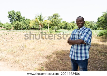 Content black African farmer is standing in front of a newly acquired, unplanted piece of land, intended for growing vegetables