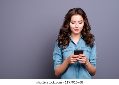 Content calm trendy nice cute adorable lovely attractive brunette caucasian girl with wavy hair in casual denim shirt, playing game in phone, isolated over grey background