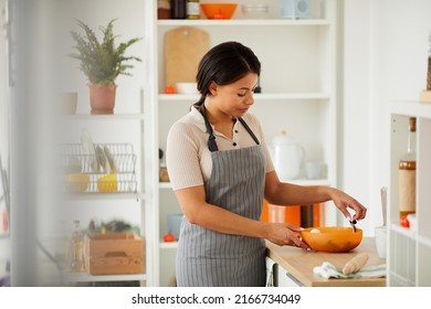 Content Careful Young Black Woman In Apron Standing At Kitchen Counter And Mixing Ingredients In Plastic Bowl