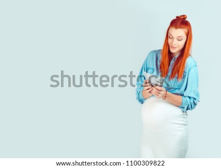 Content casual woman waiting for baby and holding pile of money for first time looking happy isolated on light blue. I received my start maternity benefit grant for pregnancy concept.