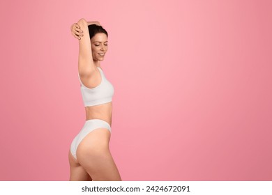 Content and composed, european young woman with closed eyes raises her arms above, showcasing a serene moment in a snug white sports top and bikini on a pink background, studio - Powered by Shutterstock