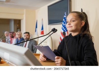 Content Confident Little Eco Activist In Black Sweater Standing At Rostrum And Reading Report At Political Conference