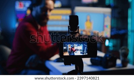 Content creation equipment used by photo editor to film tutorial on selecting editorial pictures for fashion magazine. Focus on camera recording photographer in blurry background presenting his work