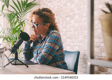 Content creator adult woman recording a podcast interview using microphone and laptop sitting at the desk. Home office workstation and smart working modern people lifestyle. Online radio computer job