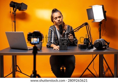 Content creator holds up a microphone while discussing a professional videographer camera battery during a podcast recording in a home studio, linking podcast studio and camera gear.