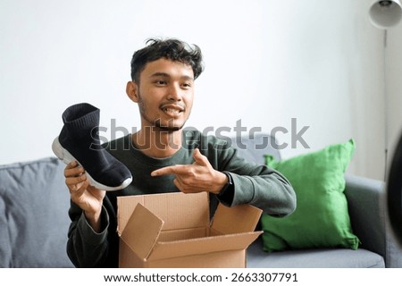 Content Creator Sitting On Sofa Showing Product In Cardboard Box To His Audience