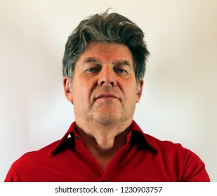 Content Handsome Older Man In Red Shirt Sitting And Watching The Camera Really Isolated Over White Background