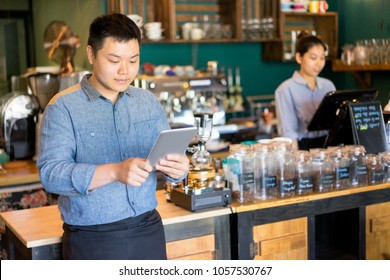 Content Handsome Young Cafe Employee Using Tablet As Personal Organizer To Add New Orders. Busy Coffee Shop Manager Viewing Report. Small Business Concept