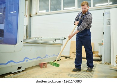 Content Handsome Young Man In Workwear Using Broom While Sweeping Floor In Dusty Factory Shop