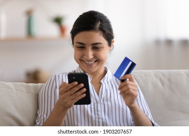Content indian woman remote worker sit on couch at home check online bank account via mobile app glad getting salary payment on card. Happy young hindu lady making successful cashless payment by cell
