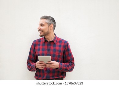 Content Man With Digital Tablet Looking Aside. Handsome Happy Bearded Man Holding Tablet Computer And Looking Away On Grey Background. Wireless Technology Concept