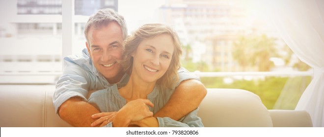 Content-Mann umarmt seine Frau auf dem Sofa und lächelt zu Hause im Wohnzimmer Kamera