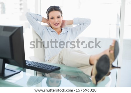 Content stylish brunette businesswoman relaxing with feet up in bright office