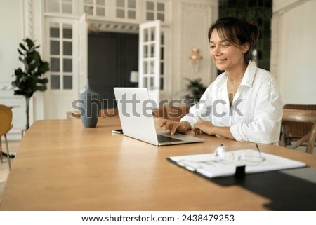 Content woman working on laptop in a well-lit room with tasteful decor, serene atmosphere.

