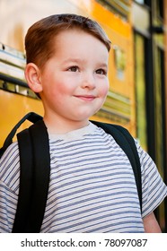 Content Young Boy In Front Of Yellow School Bus Waiting To Board On First Day Back To School.