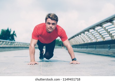 Content young man looking at camera, wearing sportswear and doing mountain climber exercise on bridge. Front view.
