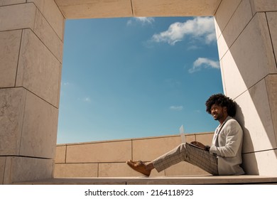 Contented African American man working in open air. Man in suit with beard using laptop. Sitting at terrace or rooftops. Working, manager, technology concept