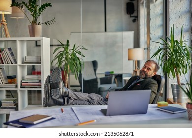 Contented Businessman Relaxing With Legs Up On Desk While Working From Home