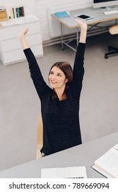 Contented Businesswoman Stretching Her Arms Above Her Head With A Pleased Smile As She Sits At Her Desk