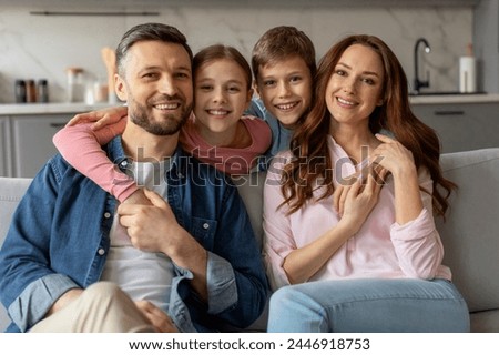A contented family of four parents, daughter and son poses with smiles for a casual portrait on their living room sofa