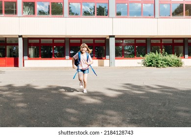 A Contented Schoolgirl With A Backpack Behind Her Back Runs From School. The Beginning Of The Holidays And The End Of The School Year. Children Study At School