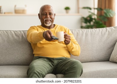 Contented Senior African American Man Watching TV Pointing Television Remote Control To Camera Switching Channels Sitting On Couch At Home. Male Viewer Enjoying Movie On Weekend - Powered by Shutterstock