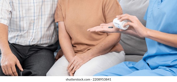 Contented Senior Woman Sit Along Side With Her Husband, Taking Medicines While Her Caregiver Advising Her Medication. Medication For Seniors, Nursing House, Healthcare At Home.