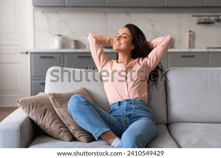 Contented young lady in casual wear with her hands behind head, reveling in serene and joyful break on a soft sofa in well-lit, stylish living room Stock photo © 