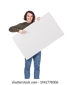 Contented Young Man Holding A Big Blank Banner For Advertising Pointing And Showing With Index Finger. Happy Guy With An Empty Sheet For Text Announcements As A Lottery Winner With Bank Check Prize