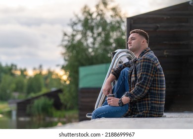 Contented young man relaxing on a wooden jetty at sunset with a cup of takeaway coffee - Shutterstock ID 2188699967