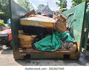 The Contents Of A Half Filled Up Dumpster. Tarp, Boards And An Old Peed Up Mattress Can Be Seen. The Dumpster Is Sitting In The Driveway Of A Suburban Home In Canada.