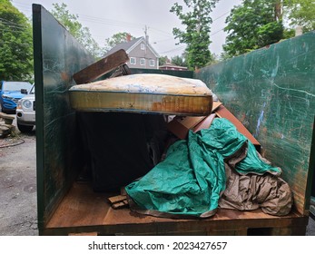 The Contents Of A Half Filled Up Dumpster. Tarp, Boards And An Old Peed Up Mattress Can Be Seen. The Dumpster Is Sitting In The Driveway Of A Suburban Home In Canada.