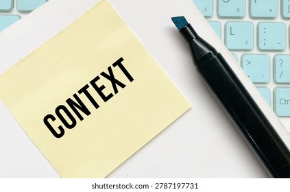 Context text on sticky note beside marker pen and keyboard on workspace desk.