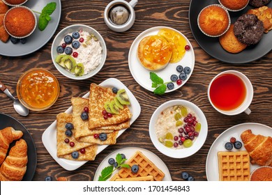 Continental Breakfast Captured From Above (top View, Flat Lay). Coffee, Tea, Croissants, Jam, Egg, Pancakes, Maffins And Oatmeal. Wooden Background. Family Breakfast Table.