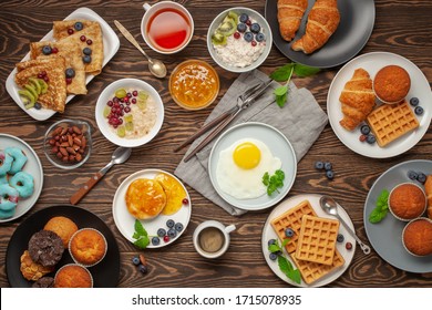 Continental Breakfast Captured From Above (top View, Flat Lay). Coffee, Tea, Croissants, Jam, Egg, Pancakes, Maffins And Oatmeal. Wooden Background. Family Breakfast Table.