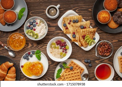 Continental Breakfast Captured From Above (top View, Flat Lay). Coffee, Tea, Croissants, Jam, Egg, Pancakes, Maffins And Oatmeal. Wooden Background. Family Breakfast Table.