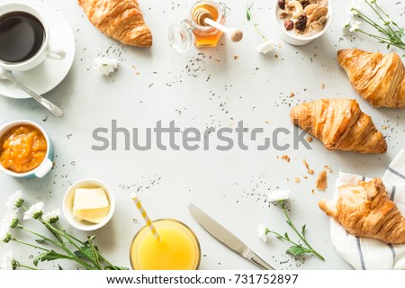 Continental breakfast captured from above (top view, flat lay). Coffee, orange juice, croissants, jam, honey and flowers. Grey stone worktop as background. Layout with free text (copy) space.
