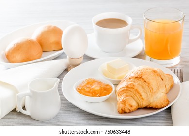 Continental breakfast with a croissant, boiled egg. Coffee or tea with milk, a glass of juice, buns, butter, jam. Soft backlight - Shutterstock ID 750633448