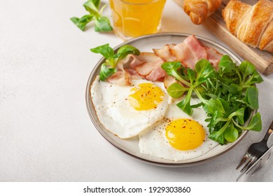 Continental breakfast - fried eggs, bacon and lettuce leaves in a plate on a bright background. Top View