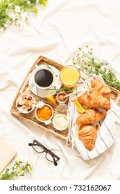 Continental Breakfast On White Bed Sheets. Coffee, Orange Juice, Croissants, Jam, Honey And Flowers On Wicker Tray From Above (top View, Flat Lay). Background Layout With Free Text (copy) Space.