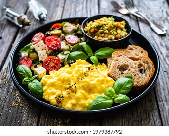 Continental breakfast - scrambled eggs, bread and greek salad on wooden table 
