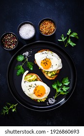 Kontinentales Frühstück - sonnige Beistelleier auf geröstetem Brot mit Avocado auf schwarzem Hintergrund
